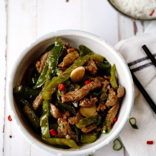 A bowl of rice with asparagus beef on top of the rice.