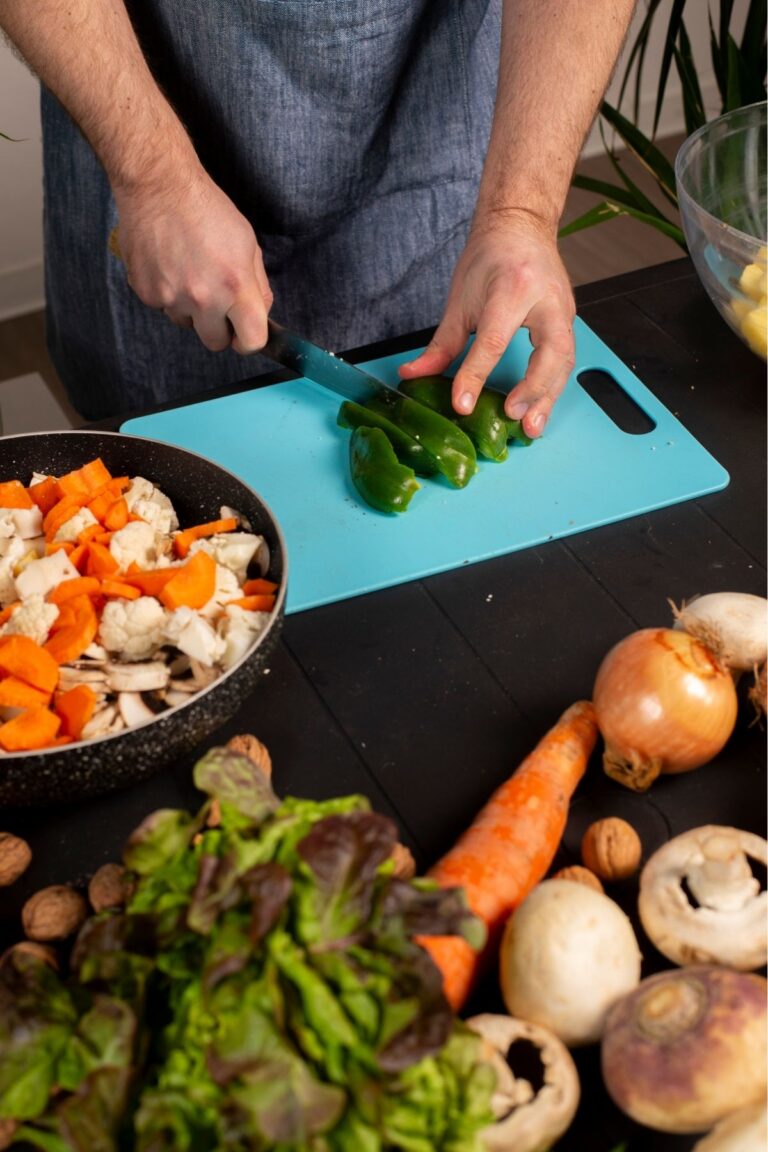 a person standing next to a counter with a cutting board in front of them while they cut vegetables