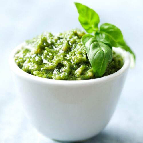 White bowl with homemade pesto in it. topped with a basil leaf.